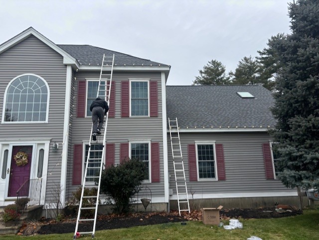 Installer on a ladder working along the roofline of a grey colonial home