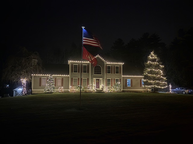 Evening home with an American flag, warm white C9 rooflines and lit trees